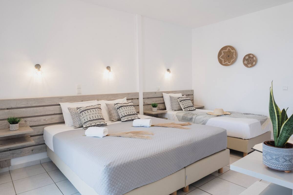 Un dormitorio moderno con dos camas, cabecero de madera, mesitas de noche con plantas e iluminación en la pared.