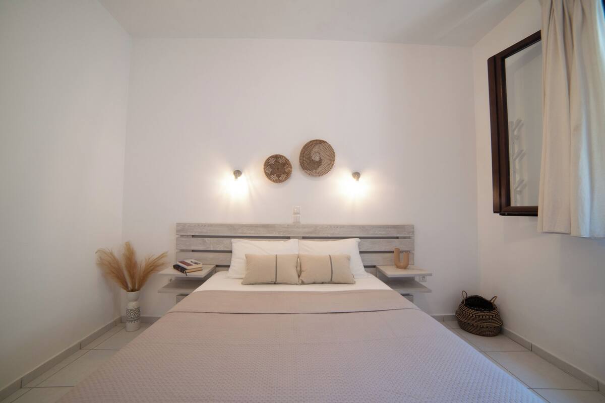 Un dormitorio con cama, mesitas de noche, luces fijadas en la pared, decoración en la pared y una ventana con cortinas.
