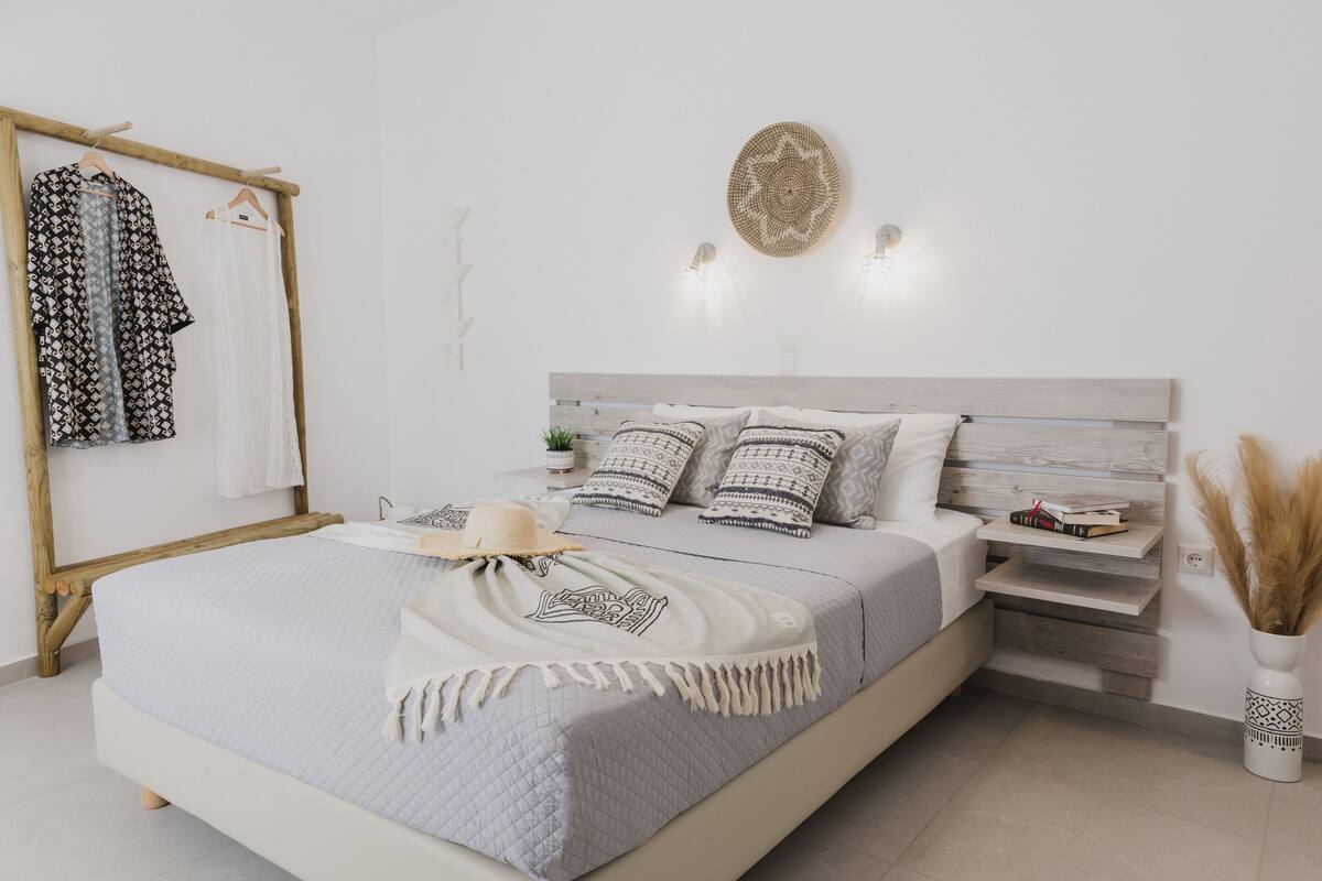 Un dormitorio con cama, mesitas de noche, estante en la pared, perchero y un adorno de pared.