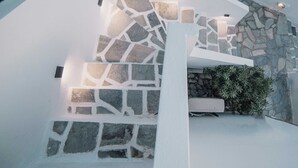 Una escalera de piedra con barandillas blancas que lleva a un muro de piedra y un pequeño arbusto verde.