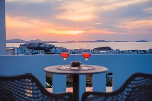 Una mesa con dos copas de vino tinto, con vistas a un pueblo costero de edificios blancos y un atardecer.