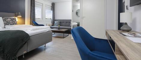 A modern hotel room with a bed, a desk, a blue armchair, and a sofa.