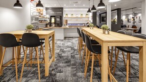 A modern cafe with wooden tables and black chairs, a juice and coffee bar, and potted plants. - Hotel Vindeus (Sodertalje)