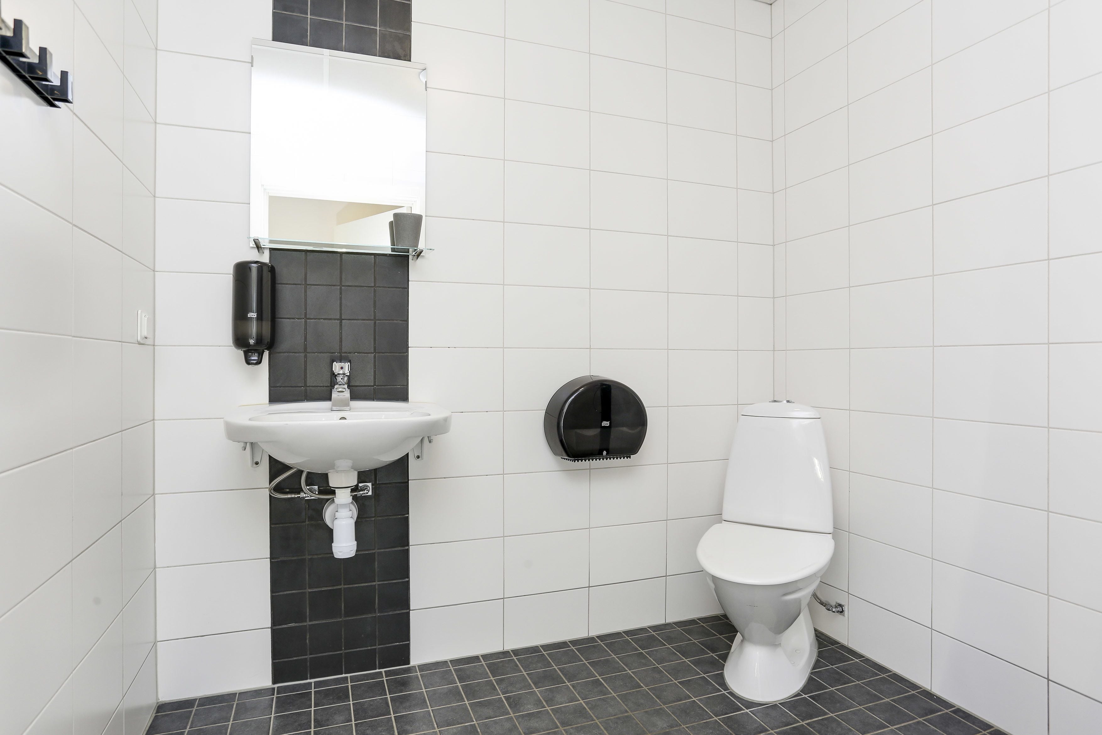 A modern bathroom with a white sink, black-tiled wall, and a toilet.