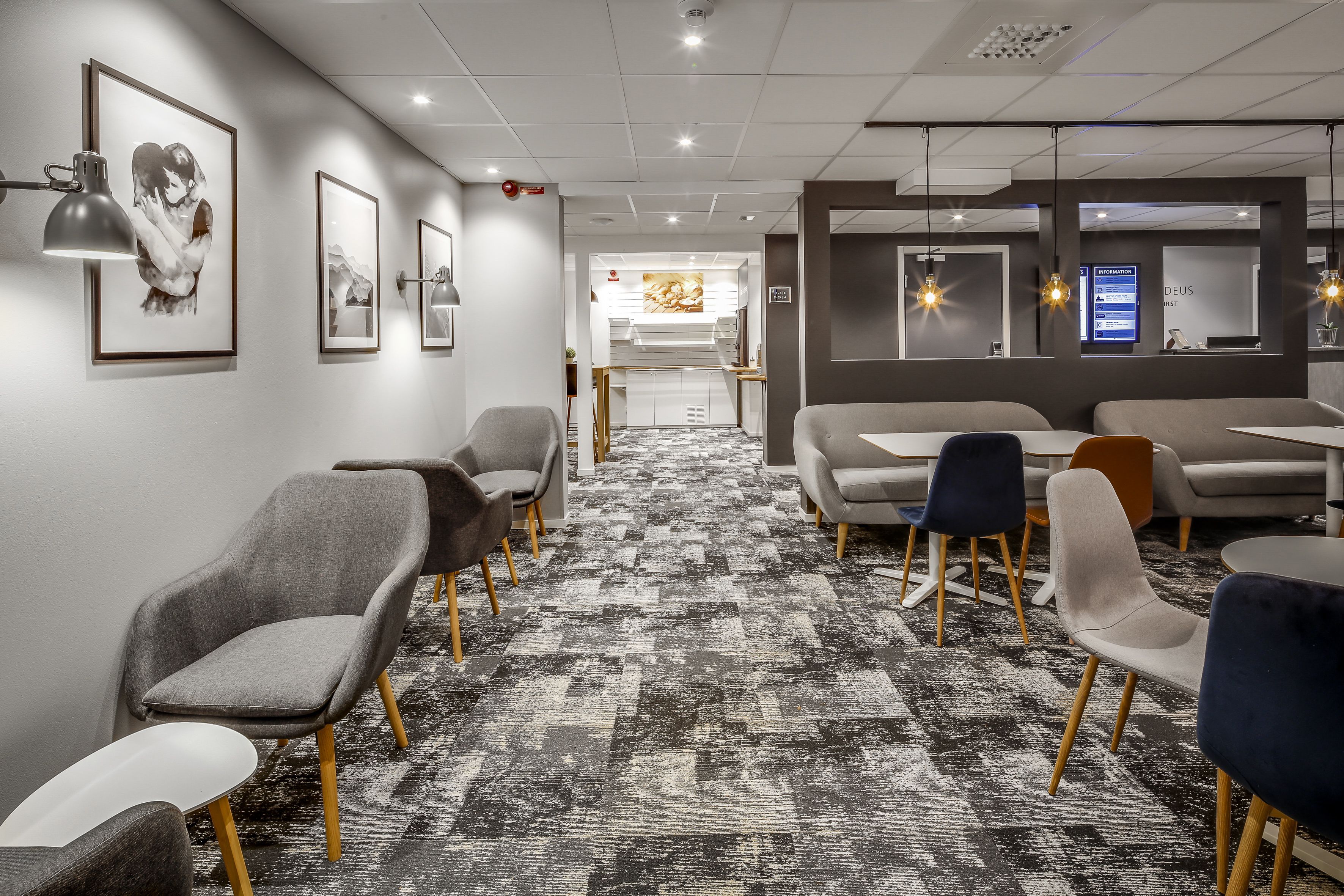 A modern hotel lobby with a patterned carpet, seating areas, framed artwork, and a reception desk.