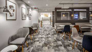 A modern hotel lobby with a patterned carpet, seating areas, framed artwork, and a reception desk.