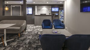 A hotel reception area with a reception desk, seating area, and a snack machine. - Hotel Vindeus (Sodertalje)