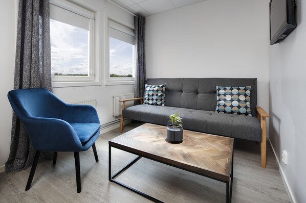 Una sala de estar moderna con un sofá gris, un sillón azul y una mesa de centro de madera con una planta.