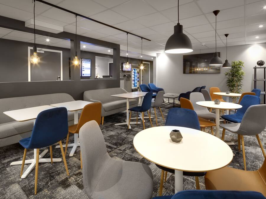 A modern lounge area with seating arrangements including sofas and tables, a coffee machine, and a television screen.