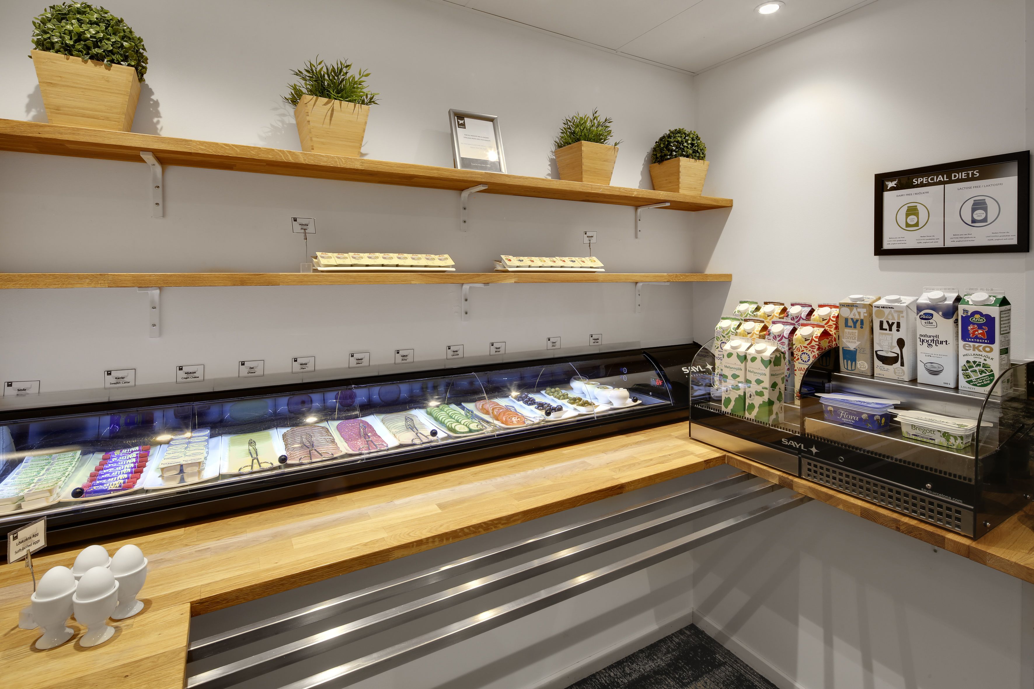 Un expositor refrigerado con diversos productos lácteos, estantes de madera con plantas en macetas y una sección con bebidas envaseladas.