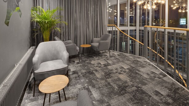 A modern lounge with grey armchairs, a small round table, and a large potted plant. - Hotel Vindeus (Sodertalje)