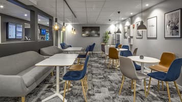 Un espace de bureau moderne avec un canapé gris, des chaises bleues et marron, une table blanche et un tapis à motifs.
