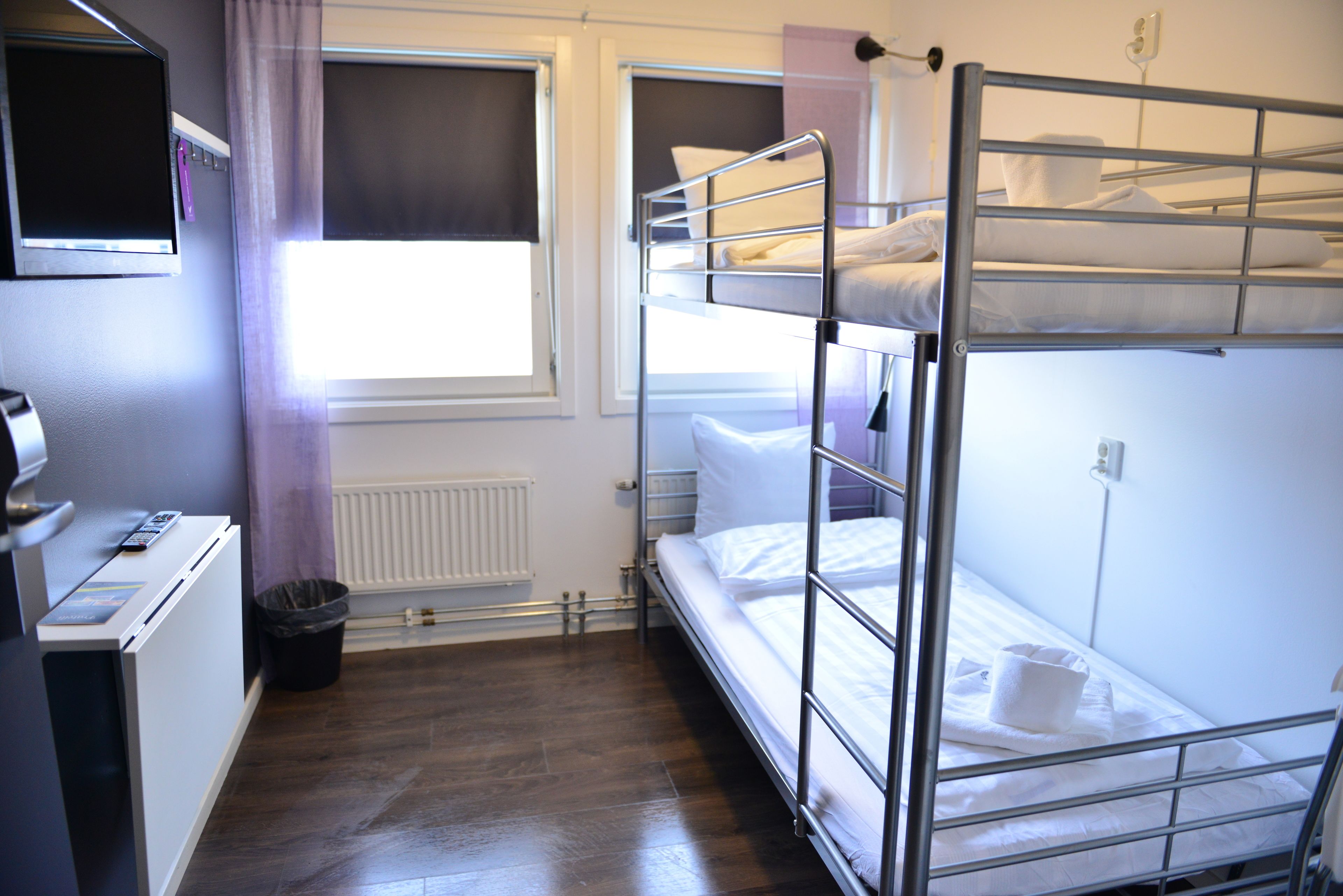A bunk bed room with a desk, a window with curtains, and a radiator.