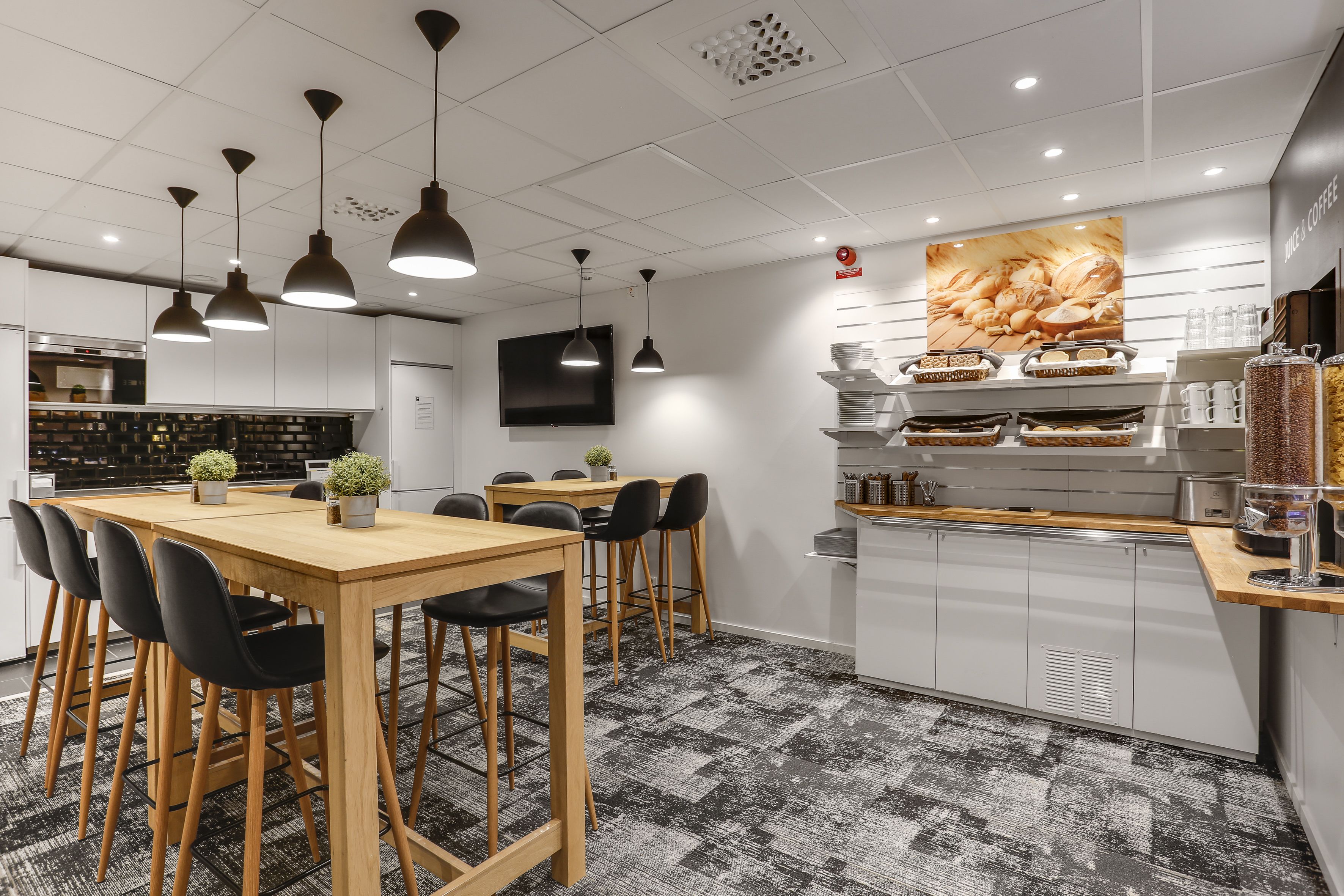 A modern kitchen with a wooden table and chairs, a coffee station, and a large wall-mounted television.