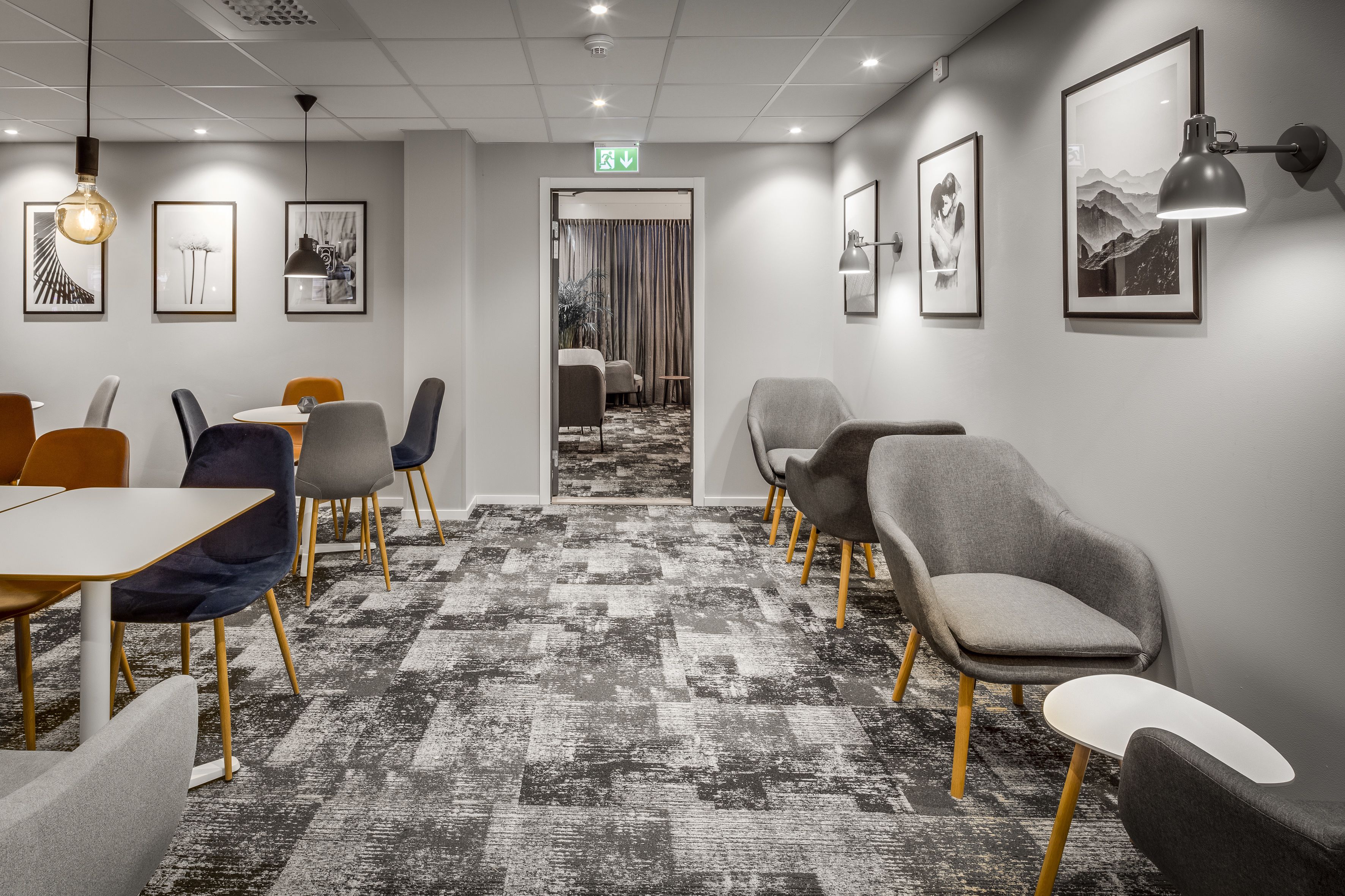A modern conference room with a patterned carpet, grey and orange chairs, and framed artwork on the walls.