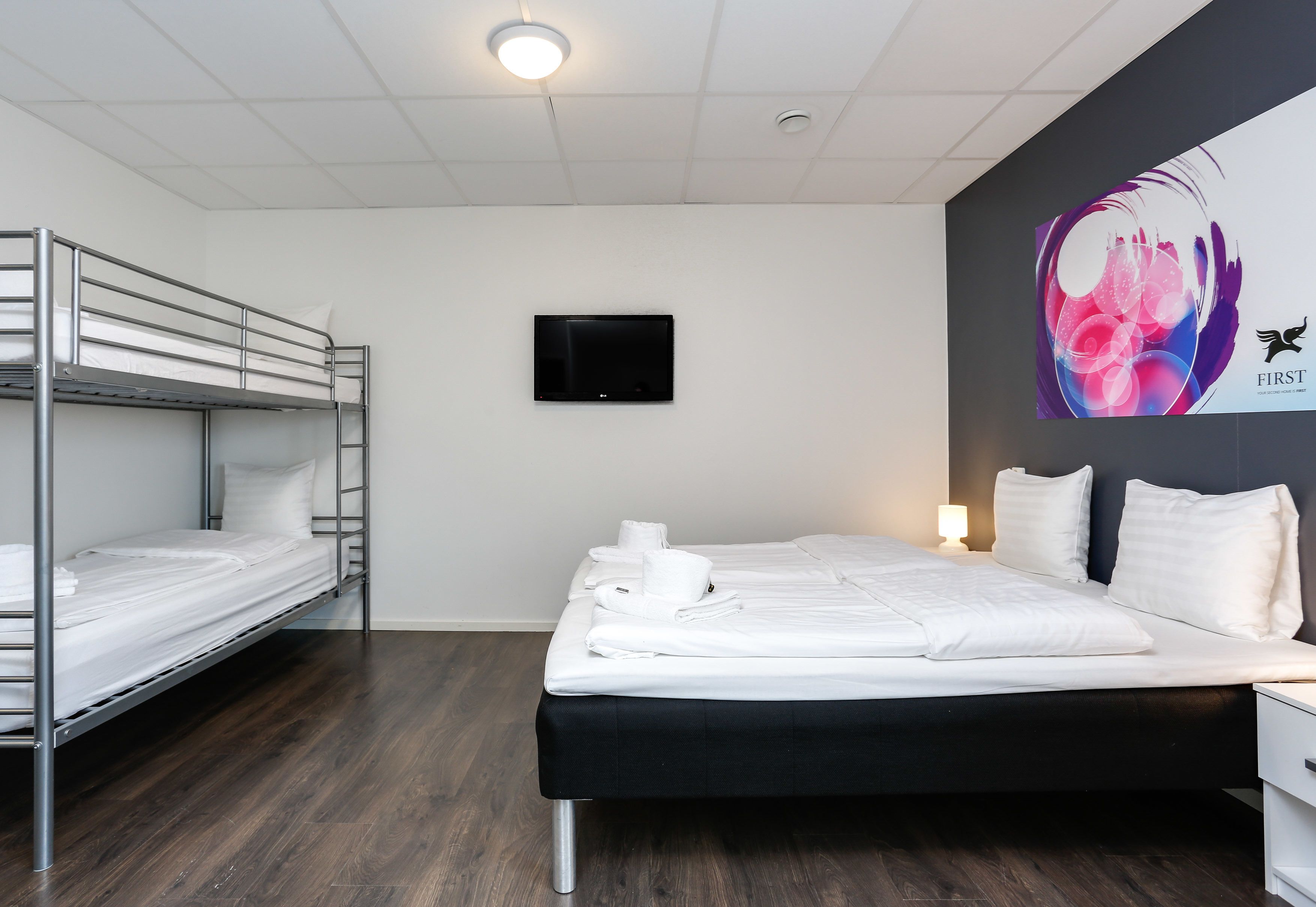 Una habitación de hotel con literas, una cama individual, un televisor de pantalla plana y una pared con diseño floral.