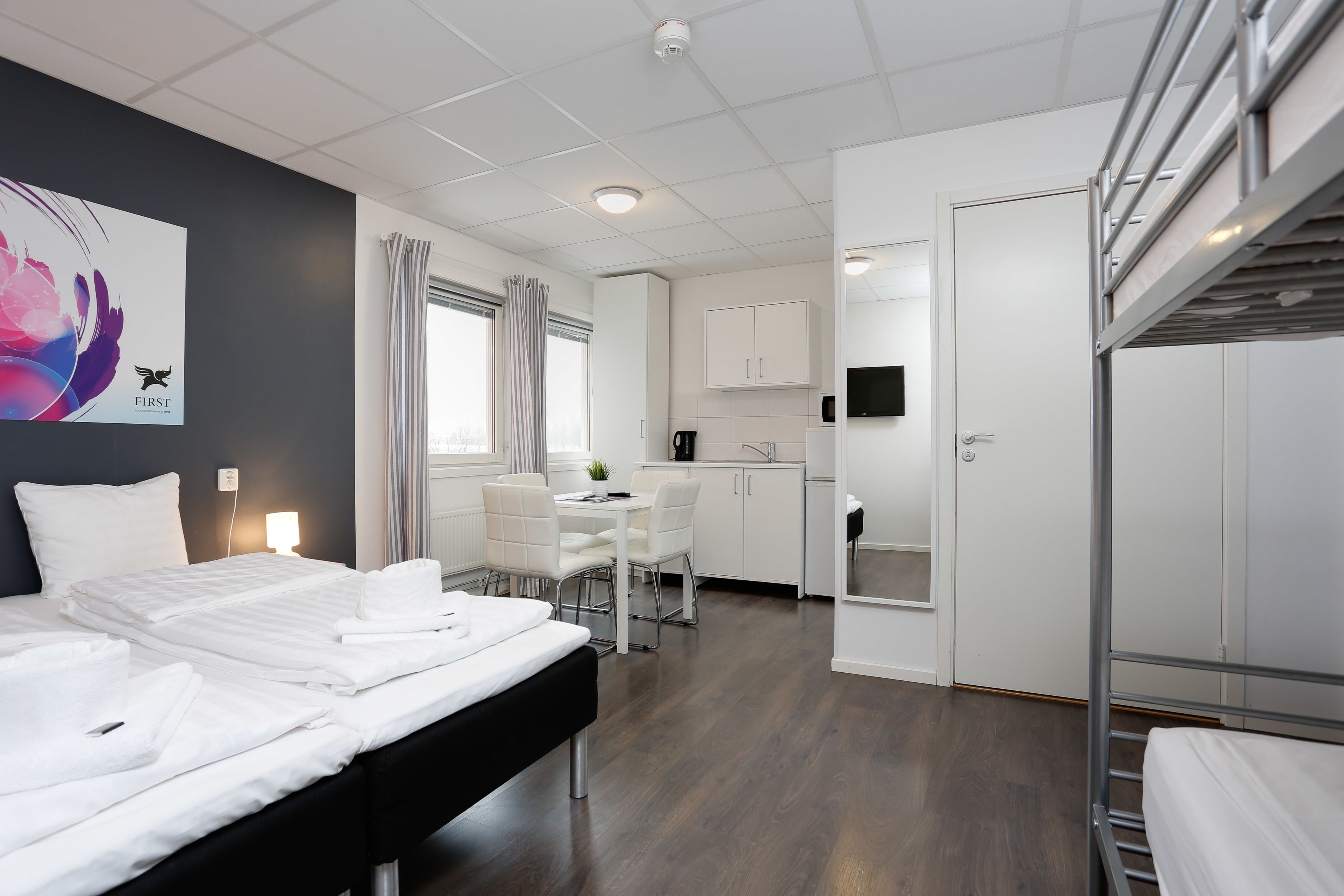Ett modernt hotellrum med en säng, ett skrivbord, en stol, ett litet kök och en TV.