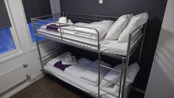 Habitación con literas, ropa de cama blanca, una ventana con persianas y un radiador.