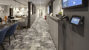 A reception area with a digital screen displaying a taxi booking service, a phone, and a reception desk. - Hotel Vindeus (Sodertalje)