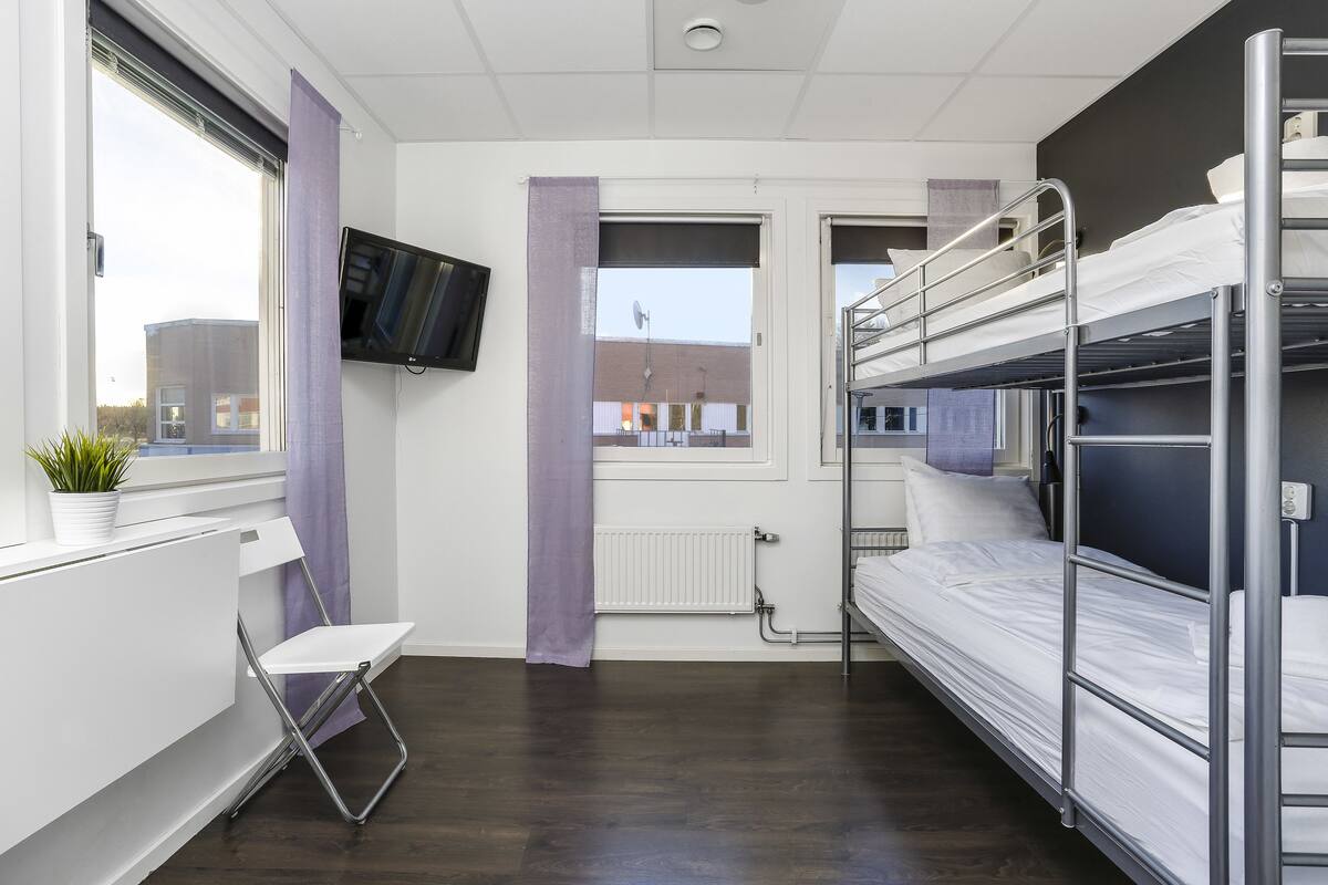 Una habitación de hotel moderna con literas, un televisor de pantalla plana, una ventana con vistas a edificios y un radiador.