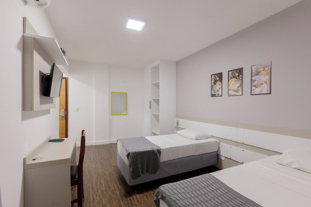 A modern hotel room with a desk, two beds, a TV, and artwork on the wall.