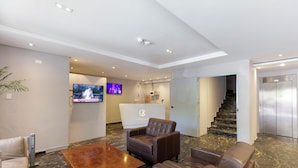 A modern lobby with leather seating, a reception desk, a TV, and an elevator. - Hotel Cardim Plaza (São Paulo)