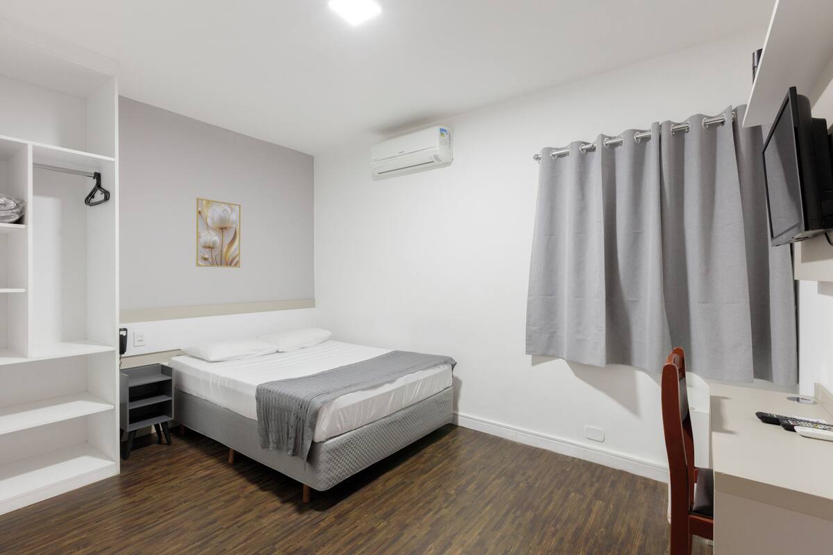 A bedroom with a bed, a desk, a chair, a TV, an air conditioner, and a wardrobe.