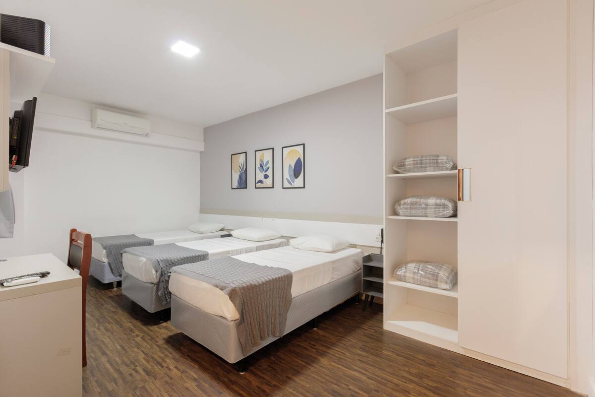 A hotel room with two beds, a desk, a chair, a wardrobe, and a TV.