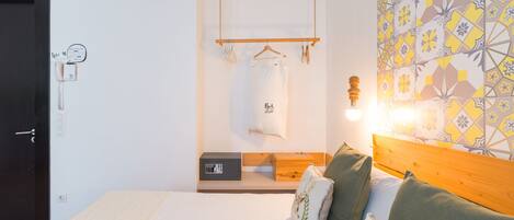 A bedroom with a bed, pillows, a hanging light, a wooden headboard, a bedside table, a wall-mounted telephone, and a patterned wall.