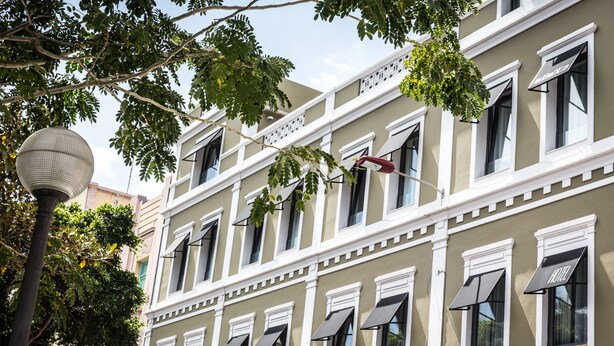 Un edificio de varios pisos con un estilo arquitectónico clásico, detalles en blanco y numerosas ventanas con toldos.