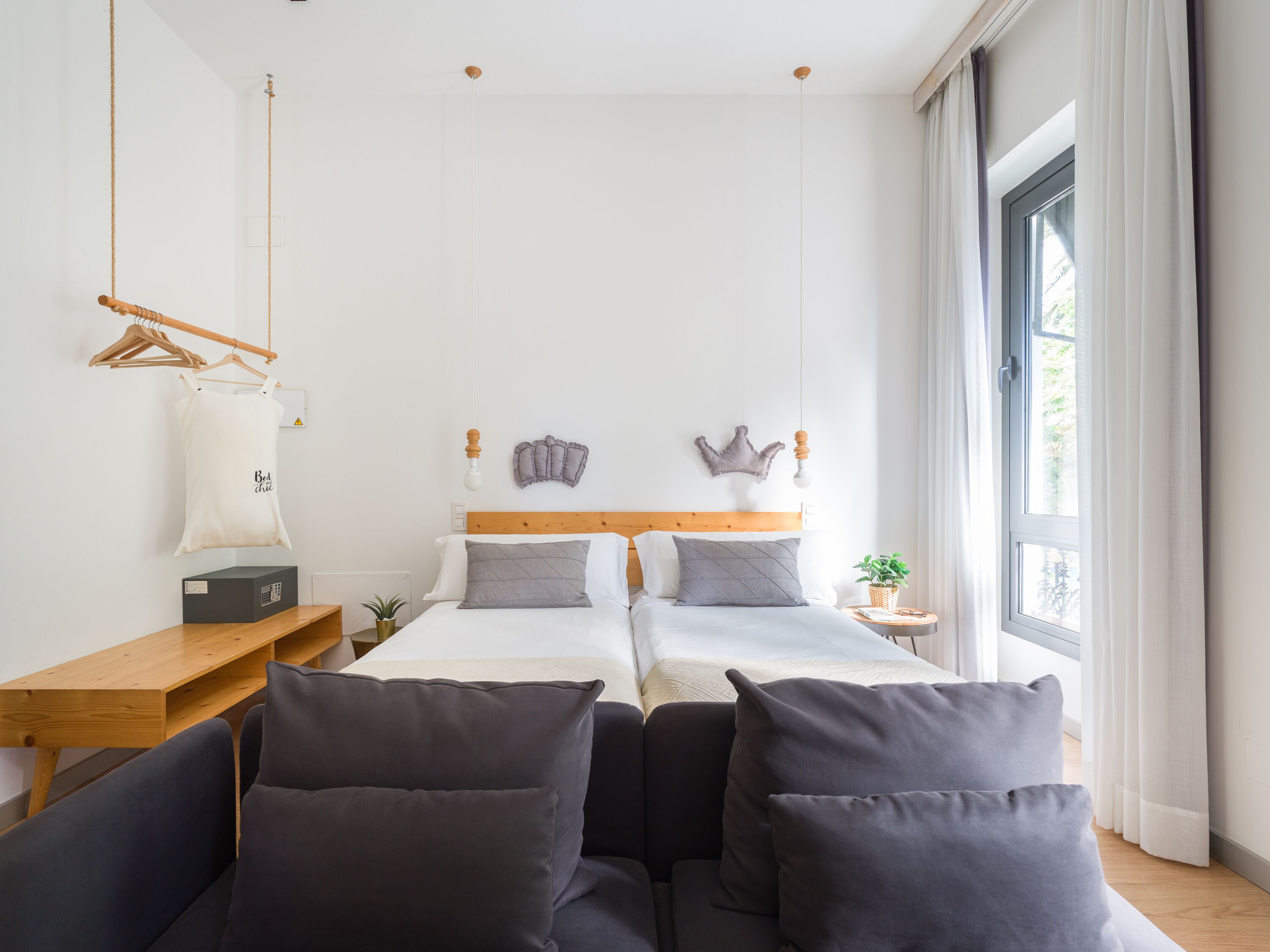 Een moderne hotelkamer met een groot bed, een houten bureau, een hanglamp en een groot raam met gordijnen.