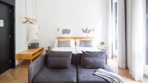 Un dormitorio moderno con una cama doble, un sofá gris, suelo de madera y ventanas amplias.