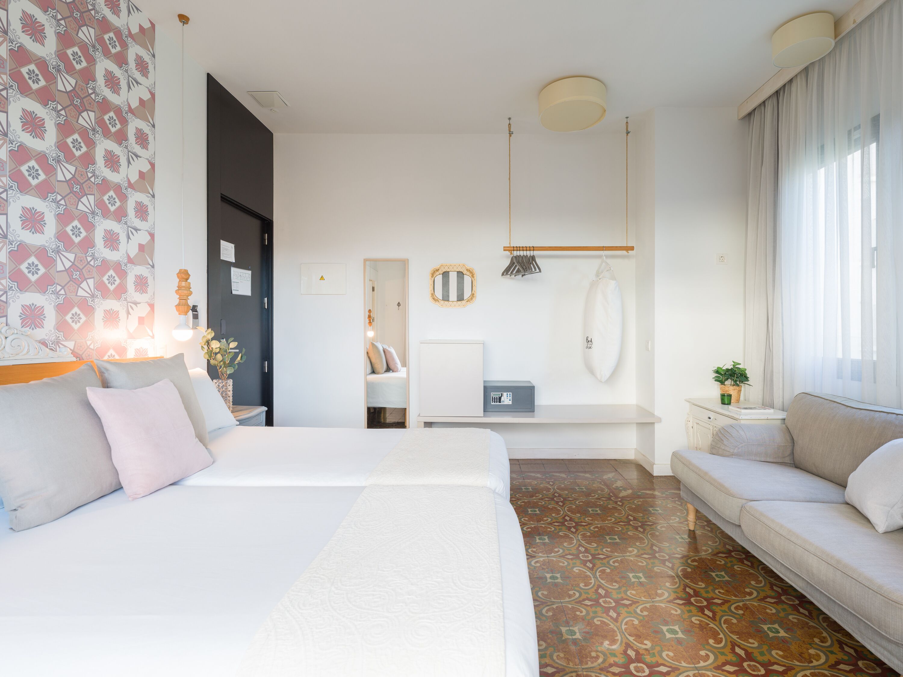 A hotel room with a large bed, a sofa, a desk, and a mirror.