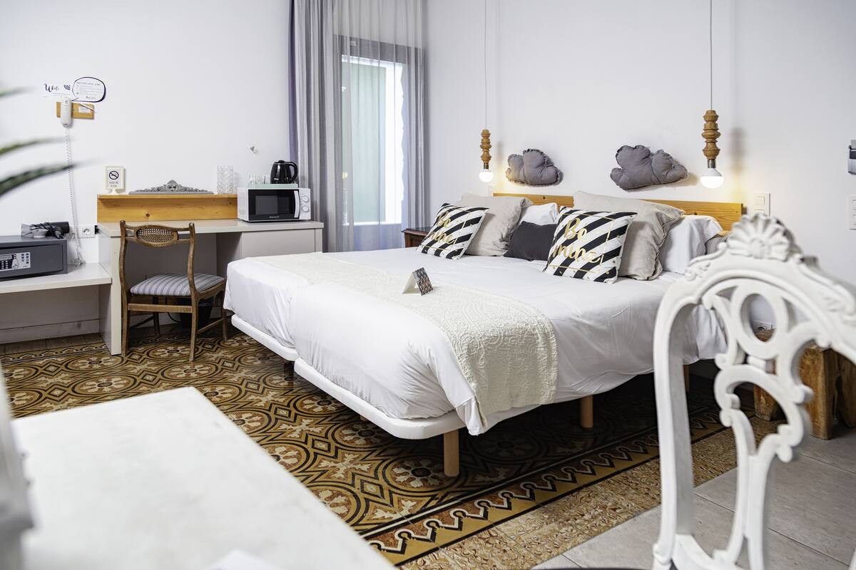 Un dormitorio con cama, escritorio, silla, microondas, teléfono y ventana con cortinas.
