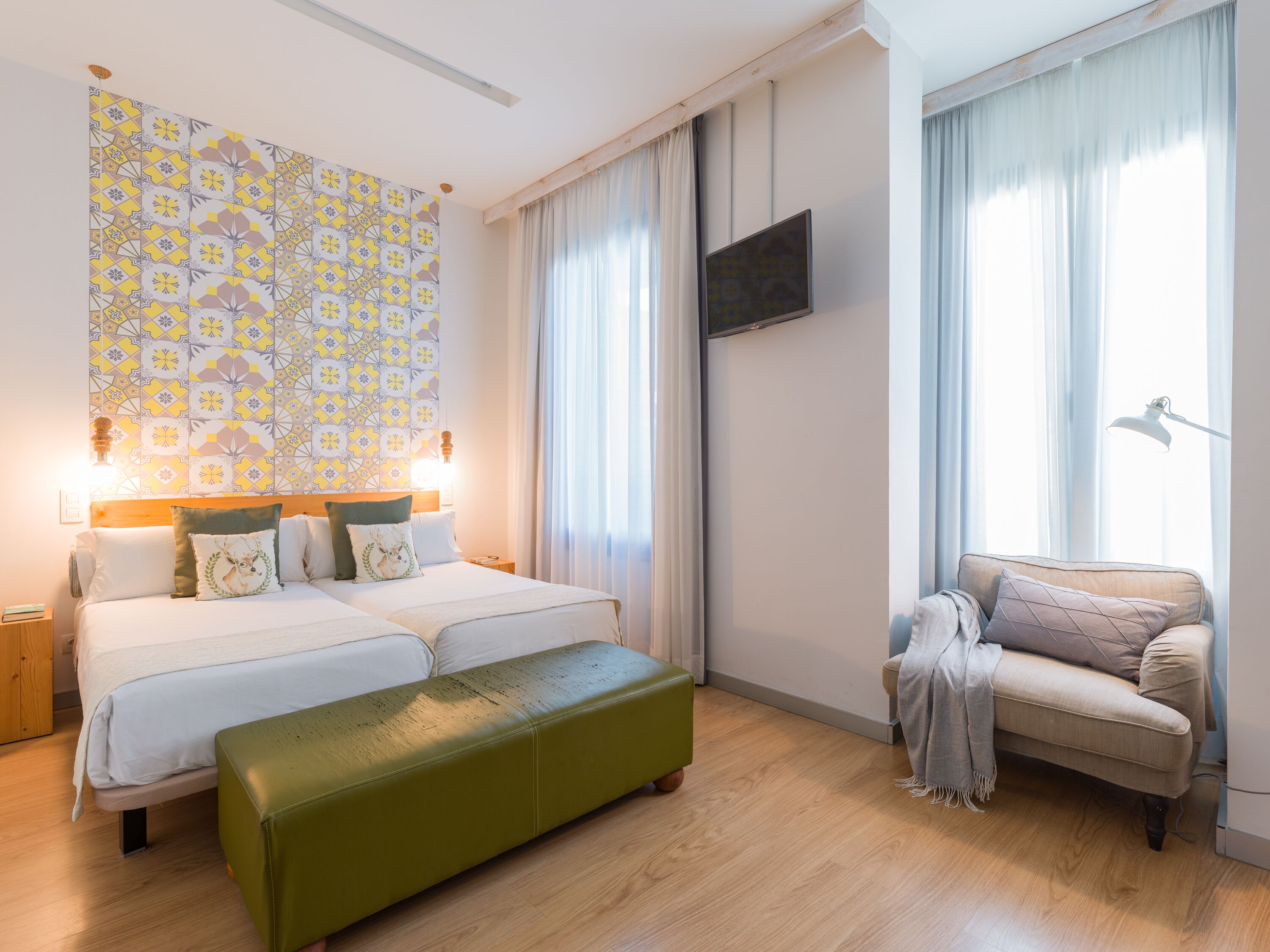 Ein Hotelzimmer mit zwei Betten, einer grünen Bank, einer Couch und einem Fernseher an der Wand.