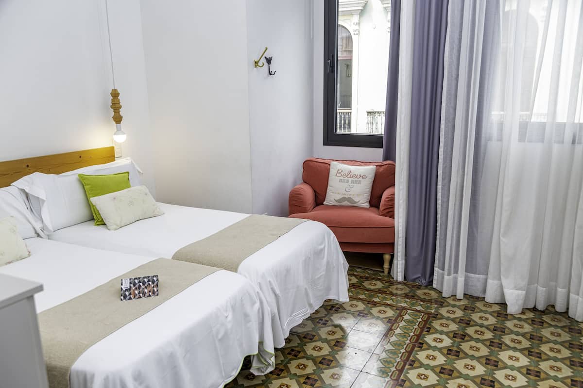 Habitación de hotel con dos camas, un sofá, un ventanal con cortinas y un suelo estampado.