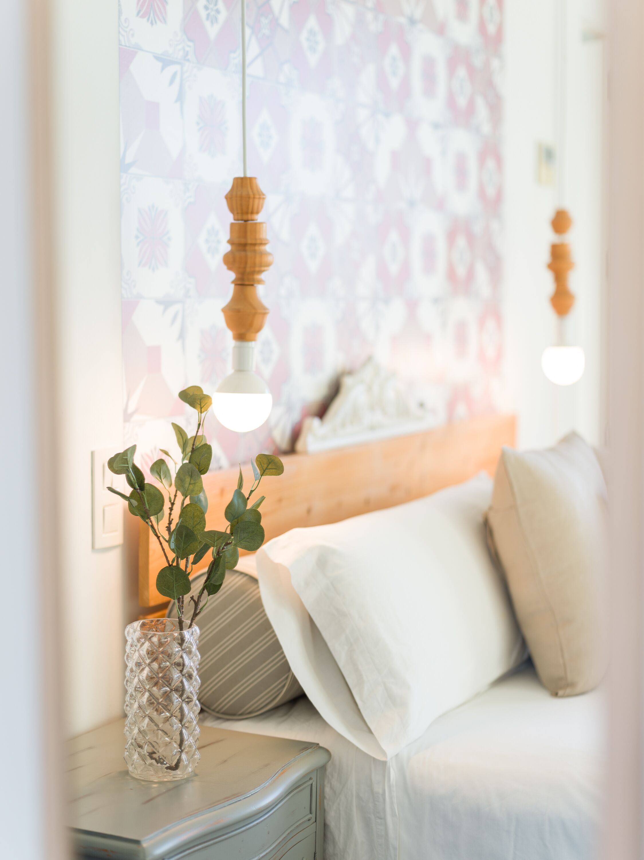 Een slaapkamer met een bed, nachtkastje en een hanglamp.