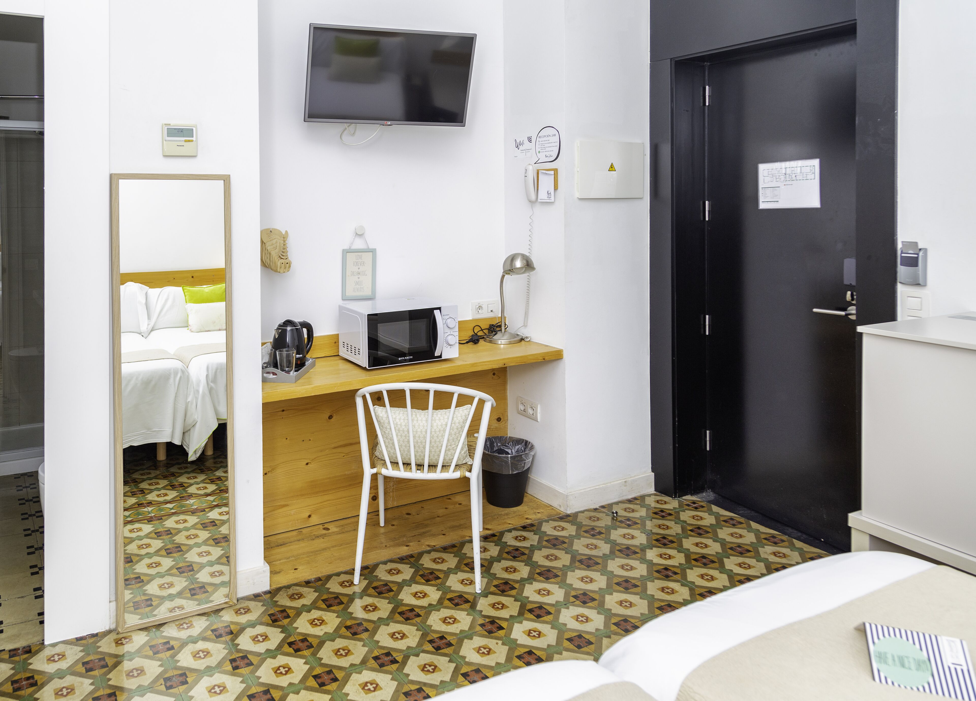 Habitación de hotel con cama, escritorio con microondas, una silla, televisión y puerta.