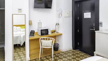Habitación de hotel con cama, escritorio con microondas, una silla, televisión y puerta.