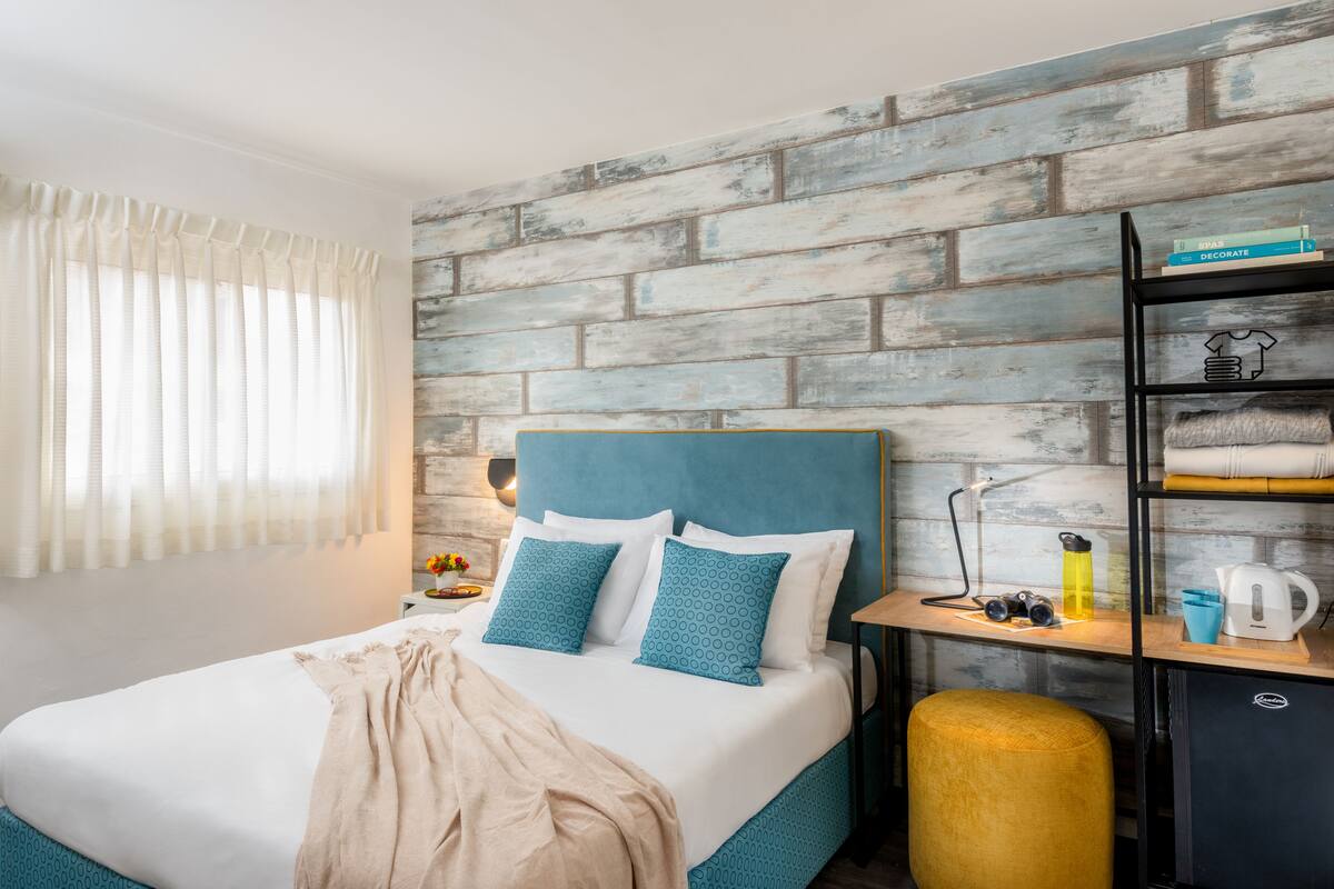 Una habitación de hotel moderna con cama, mesita de noche, armario y pared con diseño de ladrillo.