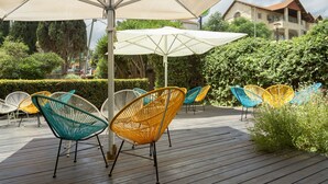 Una terrazza in legno con posti a sedere all'aperto sotto ombrelloni, circondata dal verde e con un edificio sullo sfondo.