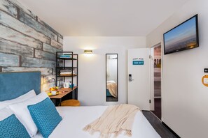 A hotel room with a bed, a desk with a chair, a mirror, a TV, and a door with a sign. - Metula TravelHotel (Metula)