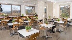 Un'ampia sala da pranzo con diversi tavoli e sedie, ampie finestre che offrono viste sull'esterno e piante in vaso che aggiungono un tocco di verde.