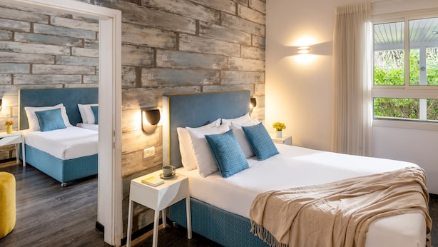 Una camera da letto moderna con parete a effetto mattone, un letto grande con biancheria blu, un comodino con una lampada e una finestra con tende.