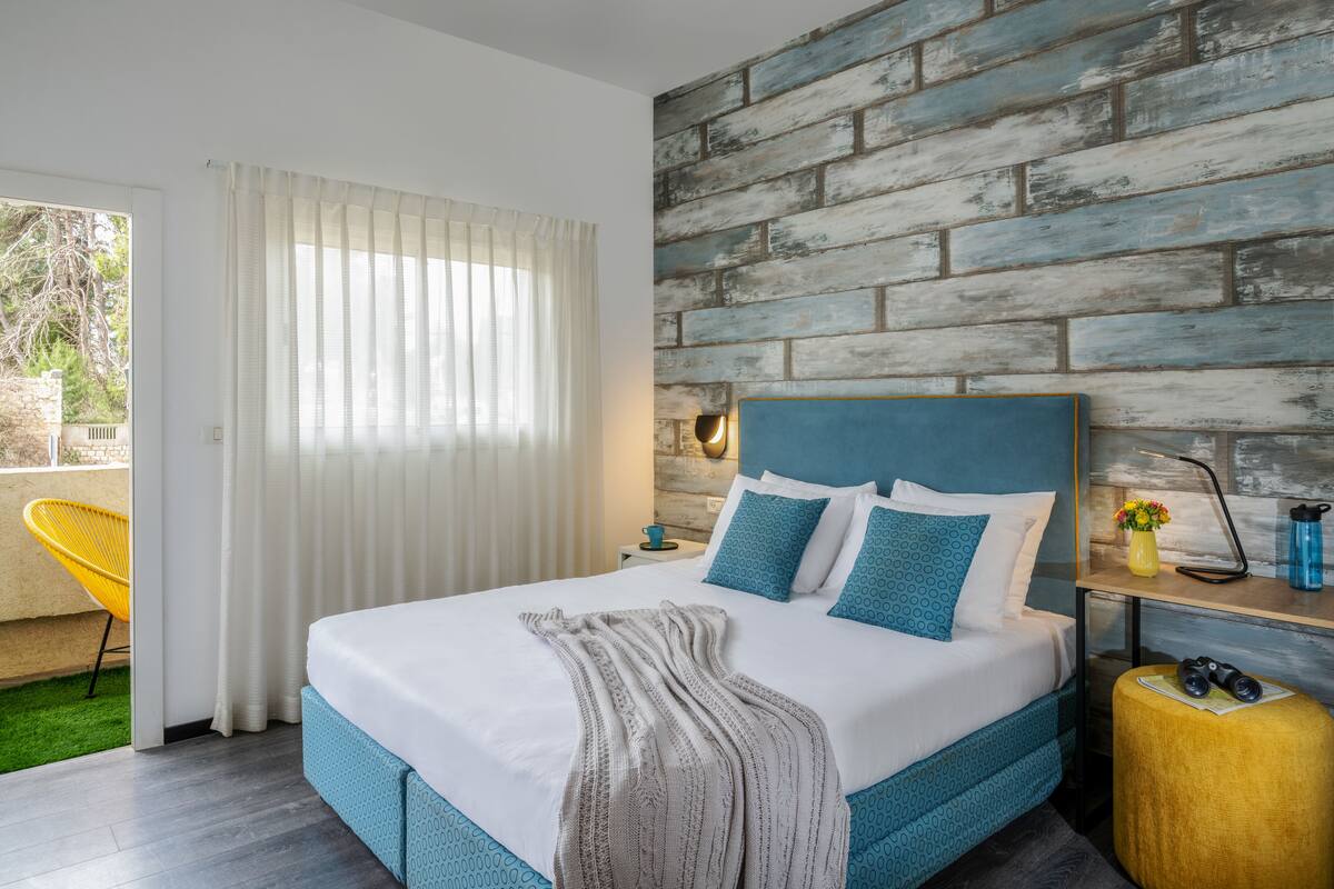 Un dormitorio moderno con una cama grande, un muro de ladrillo de madera y una silla amarilla junto a la ventana.