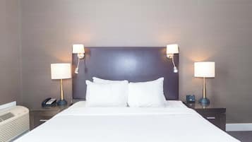 Ein ordentlich bezogenes Bett mit weißen Leinentüchern, zwei Nachttische mit Lampen, ein Nachttisch mit Telefon und einem kleinen elektronischen Gerät, und eine Wand mit strukturierter Oberfläche.