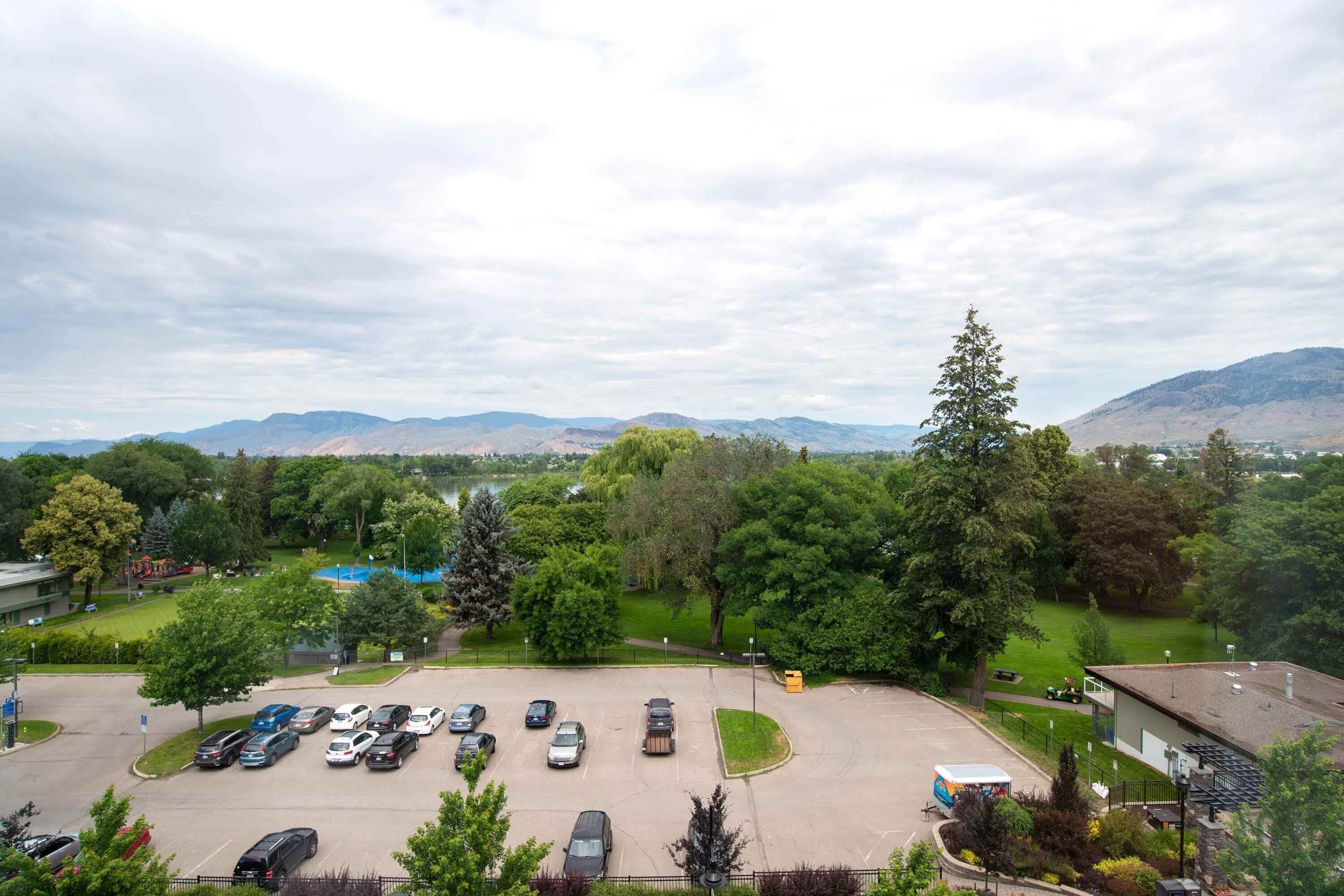 Un parking où sont garées plusieurs voitures, entouré d’arbres et offrant une vue sur des montagnes lointaines.