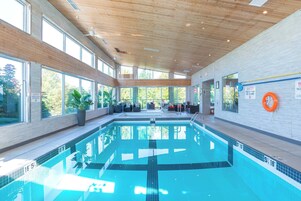 Una piscina interior moderna con agua cristalina, techo de madera y grandes ventanales.