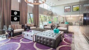A spacious living area with a large sofa, a coffee table, and a television. There are multiple seating options, including a loveseat and a chair. The room features a large window, a chandelier, and a rug with circular patterns. - Sandman Signature Kamloops Hotel (Kamloops)