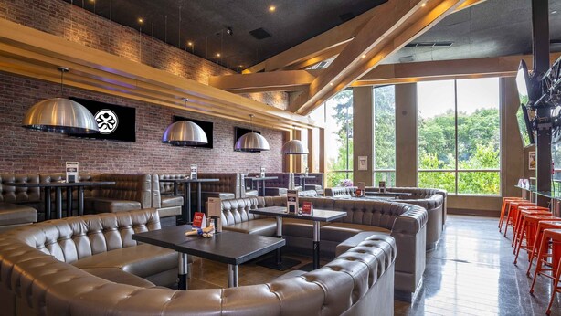 A modern restaurant with leather booths, tables, and a brick wall with hanging lights. - Sandman Signature Kamloops Hotel (Kamloops)